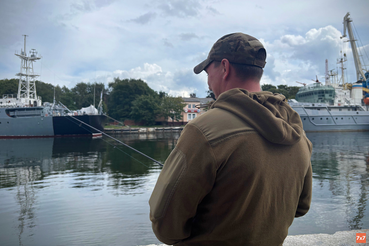 A man fishing with military ships in the background